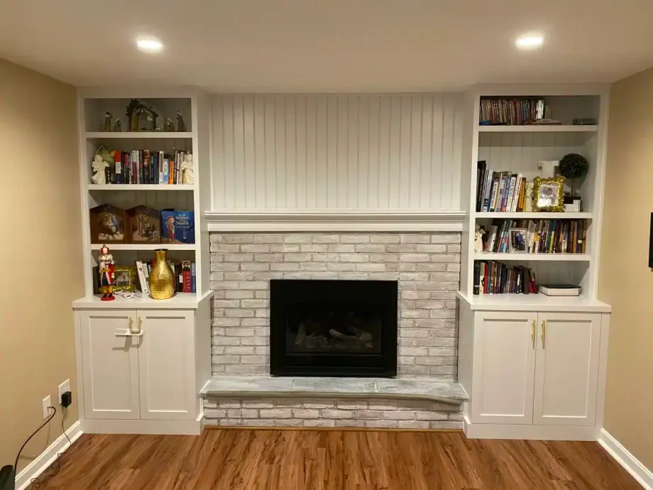 White built-in bookshelves and cabinets flanking a whitewashed brick fireplace